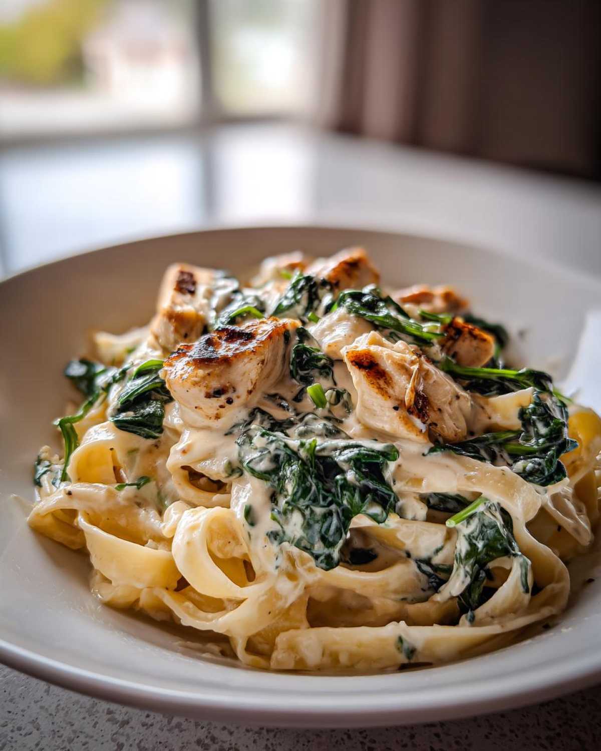 Close-up of fettuccine pasta coated in Alfredo sauce with spinach and grilled chicken pieces, perfect Creamy Spinach Chicken Pasta.