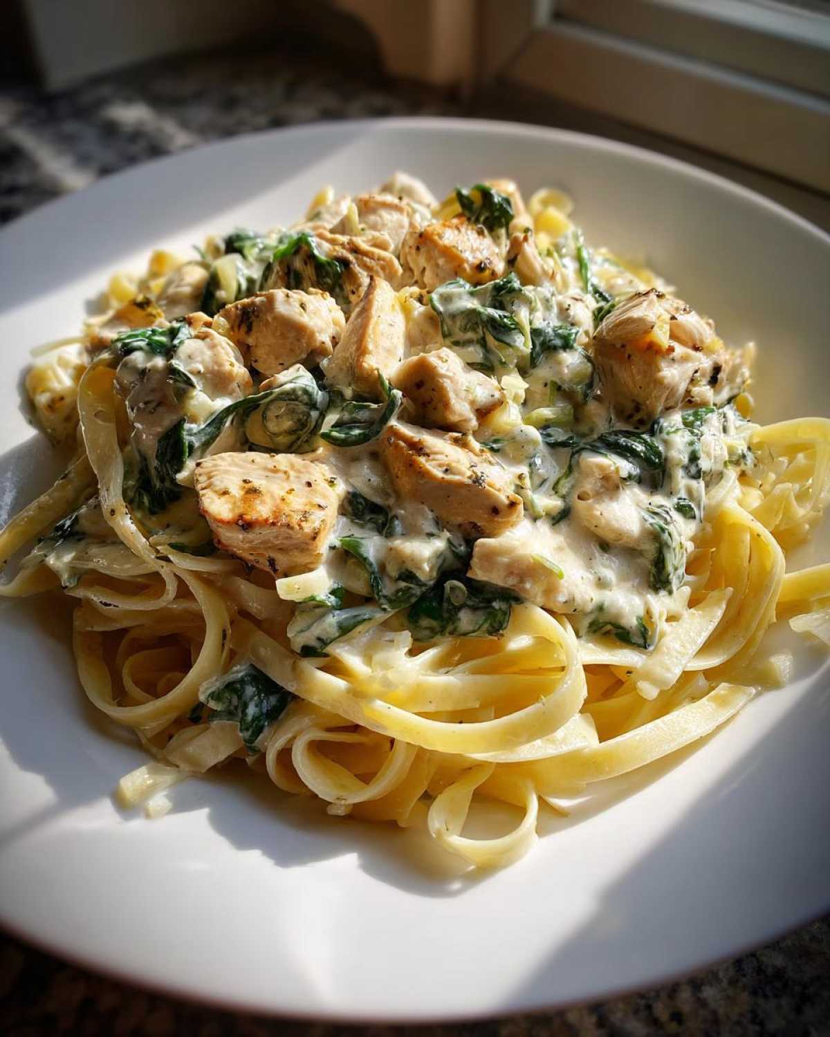 A plate of fettuccine pasta topped with chunks of seasoned chicken, spinach, and rich creamy garlic sauce, known as Creamy Spinach Chicken Pasta with Garlic.