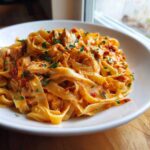 A close-up view of a white bowl filled with Creamy Sun Dried Tomato Pasta with Chicken, garnished with parsley.