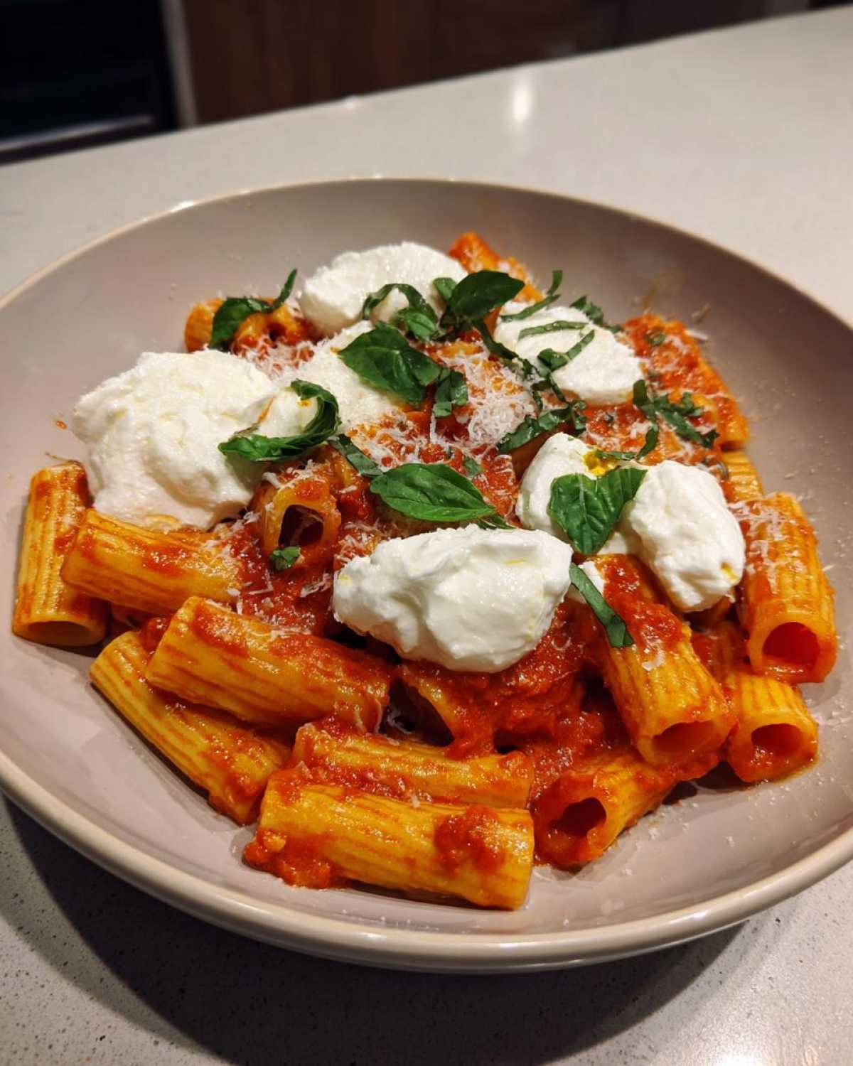 A bowl of Creamy Tomato Pasta with Burrata Cheese, topped with fresh basil leaves and grated Parmesan.