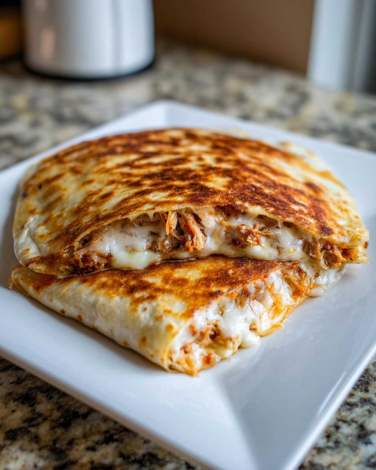 A perfectly golden and crispy Cheesy Chicken Quesadilla cut in half, showing melted cheese and shredded chicken filling.
