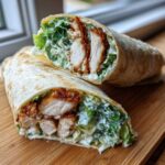 Cross-section of a Crispy Chicken Caesar Wrap showing fried chicken pieces, romaine lettuce, and creamy dressing inside a tortilla.