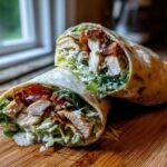 Cross-section of a Crispy Chicken Caesar Wrap showing chicken, lettuce, and creamy dressing on a wooden cutting board.