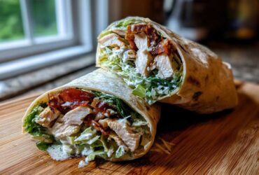 Cross-section of a Crispy Chicken Caesar Wrap showing chicken, lettuce, and creamy dressing on a wooden cutting board.