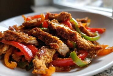 Close-up of crispy chicken fajitas strips mixed with sautéed red, green, and orange peppers on a white plate.