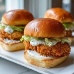 Three delicious Crispy Chicken Sliders with Garlic Sauce stacked on brioche buns with lettuce, served on a white platter.