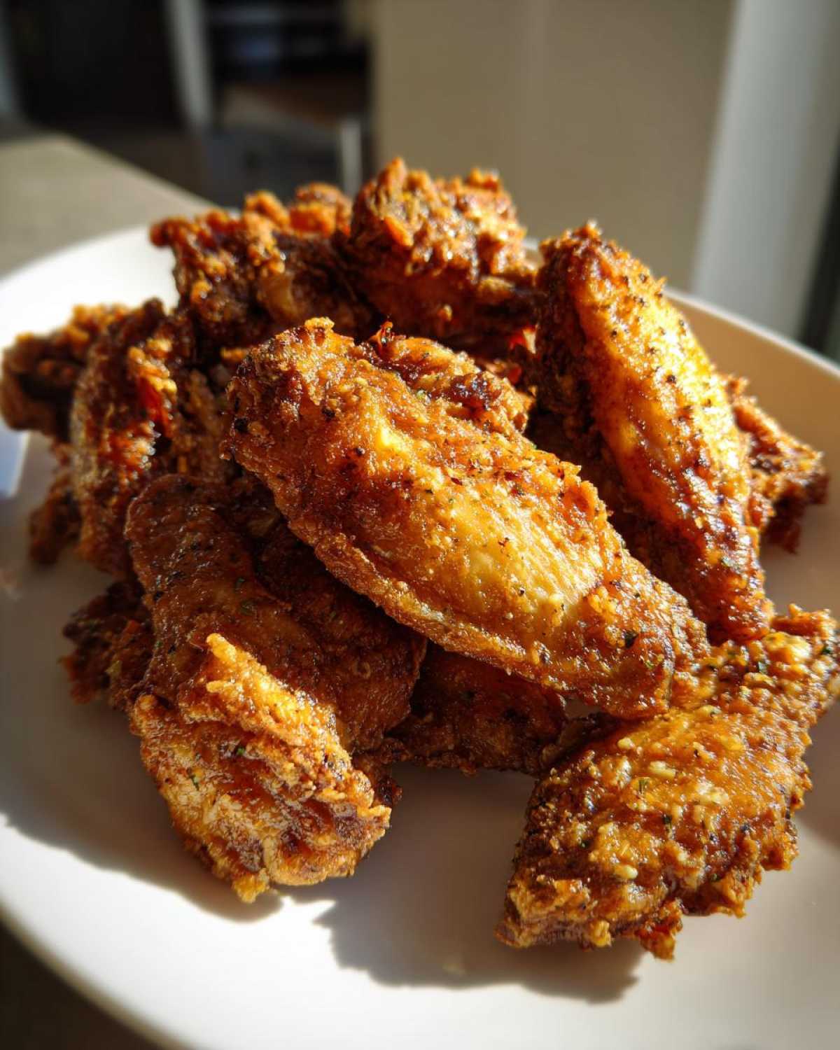 A pile of golden brown, crispy chicken wings coated in garlic parmesan sauce resting on a white plate.