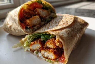 Cross-section view of a Crispy Chicken Wrap with Garlic Yogurt Sauce, showing crispy chicken, lettuce, and tomato inside a tortilla.
