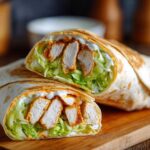 A cross-section of a Crispy Chicken Wrap with Spicy Ranch Sauce, showing crispy chicken, lettuce, and sauce inside a tortilla.