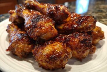A close-up of several oven-baked Crispy Honey Garlic Chicken Drumsticks piled high on a white plate.