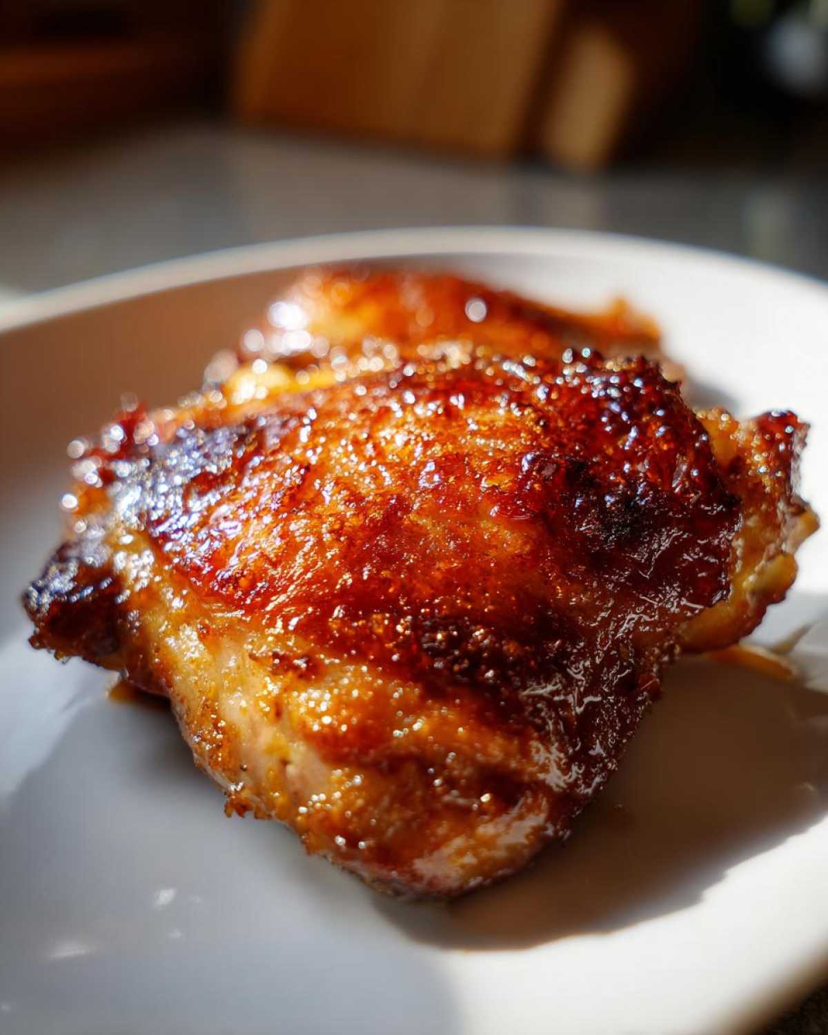 Close-up of Honey Soy Chicken Thighs with crispy, glazed, dark brown edges on a white plate.