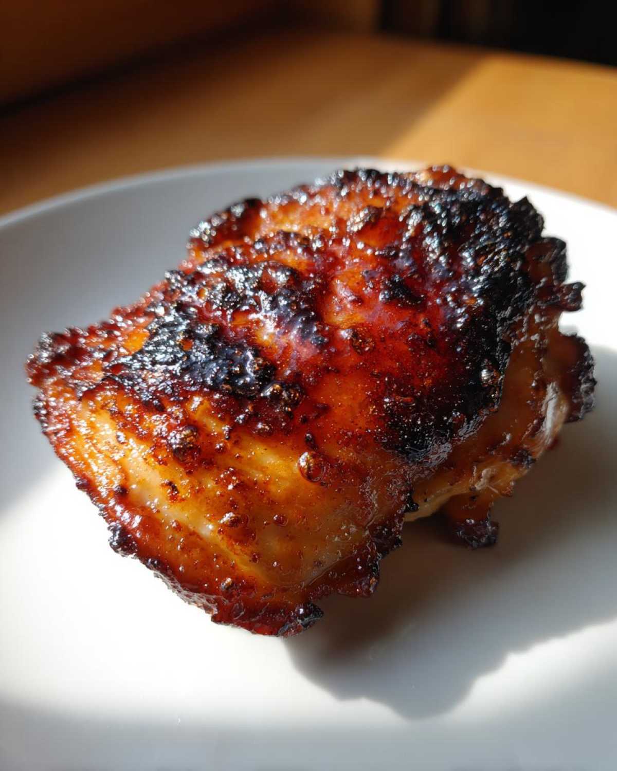 Close-up of a perfectly cooked Honey Soy Chicken Thighs with crispy, caramelized edges on a white plate.