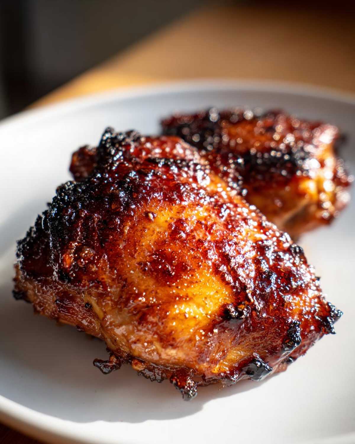 Close-up of two Honey Soy Chicken Thighs with crispy, caramelized edges on a white plate.