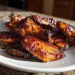 A close-up of oven baked Sticky Teriyaki Chicken Wings piled high on a white plate, glistening with sauce.