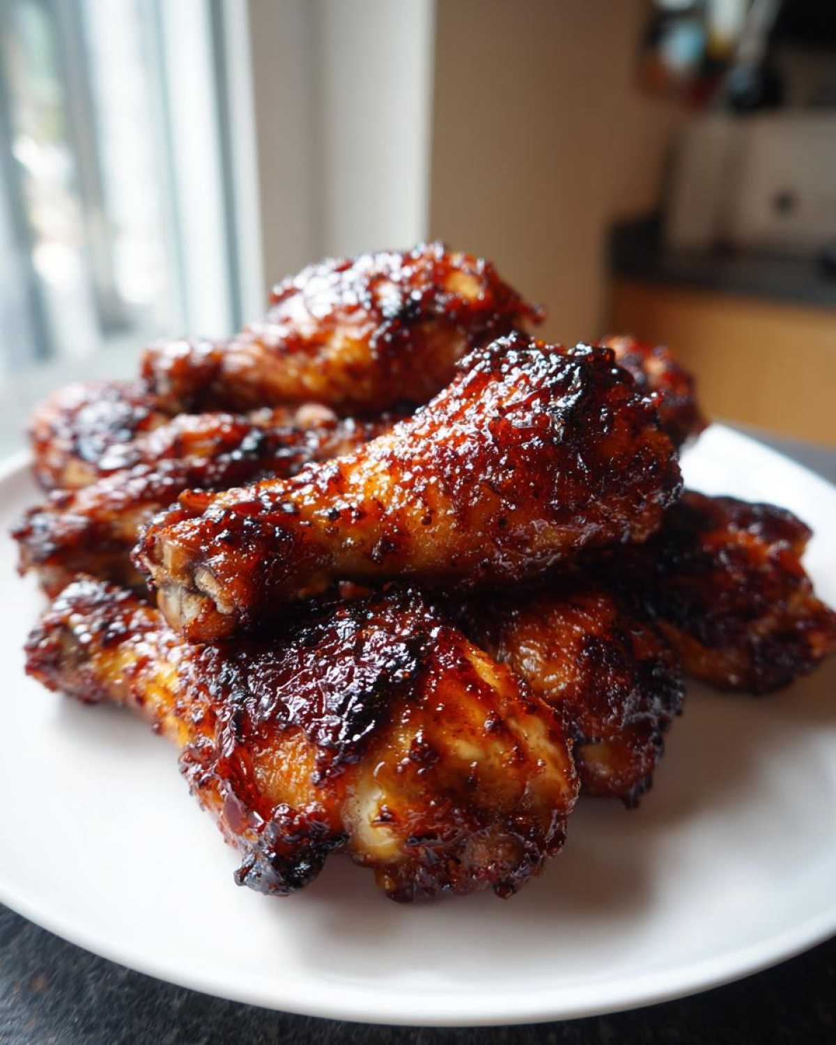 A close-up of a pile of crispy Sticky Honey Garlic Chicken Drumsticks with a dark, glossy glaze on a white plate.