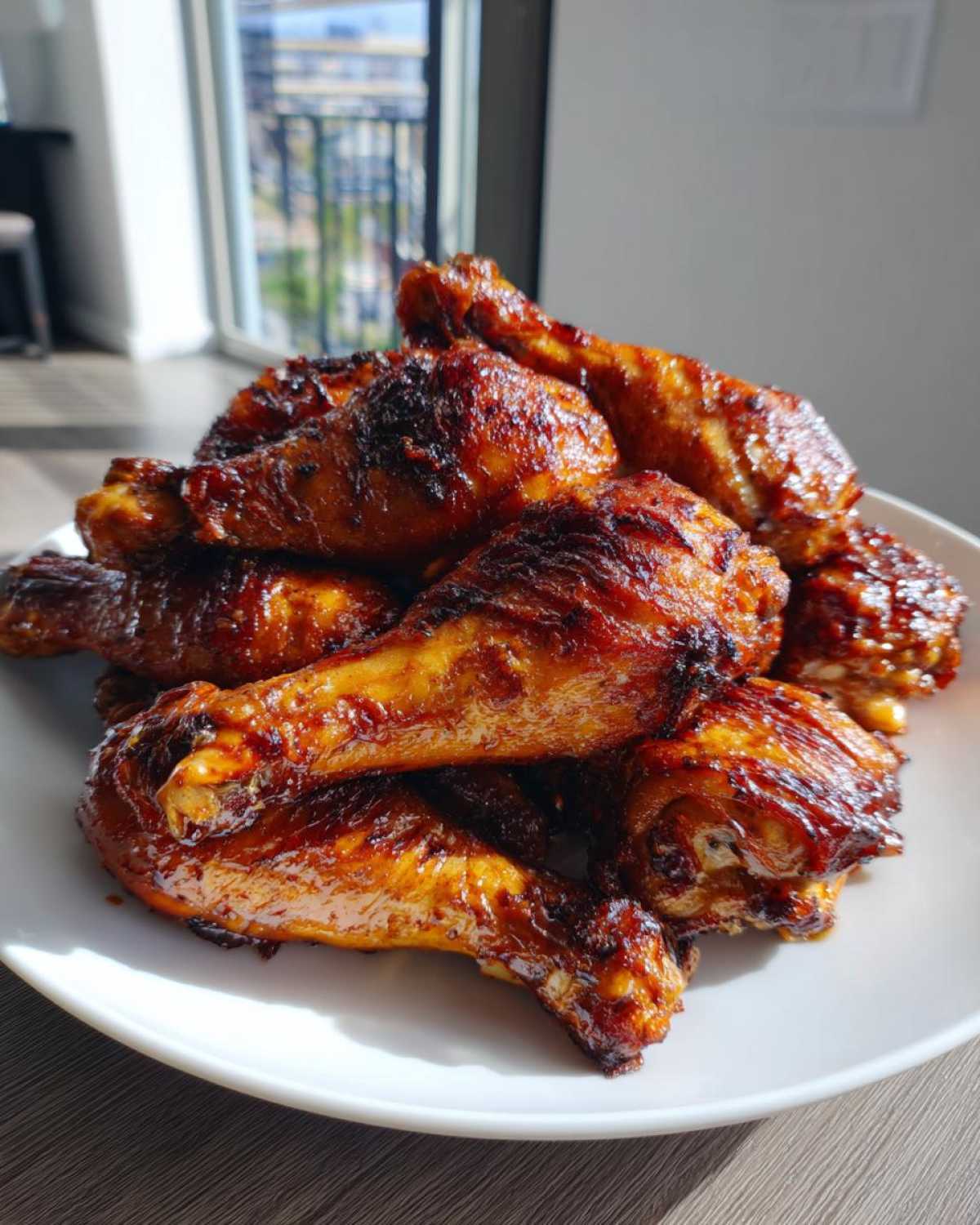 A mound of perfectly cooked, glazed Sticky Honey Garlic Chicken Drumsticks piled high on a white plate.