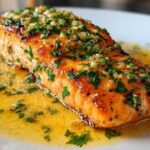 Close-up of a perfectly cooked Garlic Butter Salmon with crispy edges, topped with garlic and parsley, resting in melted butter sauce.