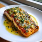 Close-up of a perfectly cooked fillet of Garlic Butter Salmon with Lemon Garlic Sauce, topped with herbs.