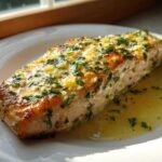 A perfectly cooked fillet of Garlic Butter Salmon with Lemon Garlic Sauce, topped with herbs.
