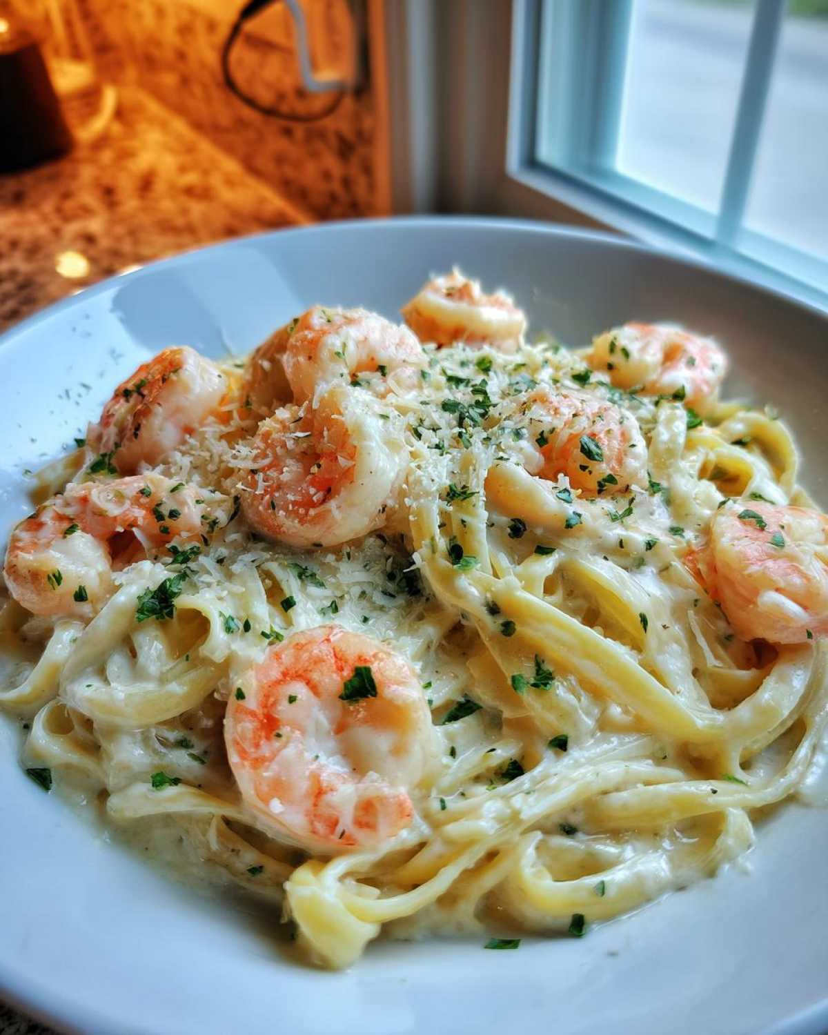 Close-up of Garlic Butter Shrimp Alfredo Pasta Creamy topped with Parmesan and parsley in a white bowl.