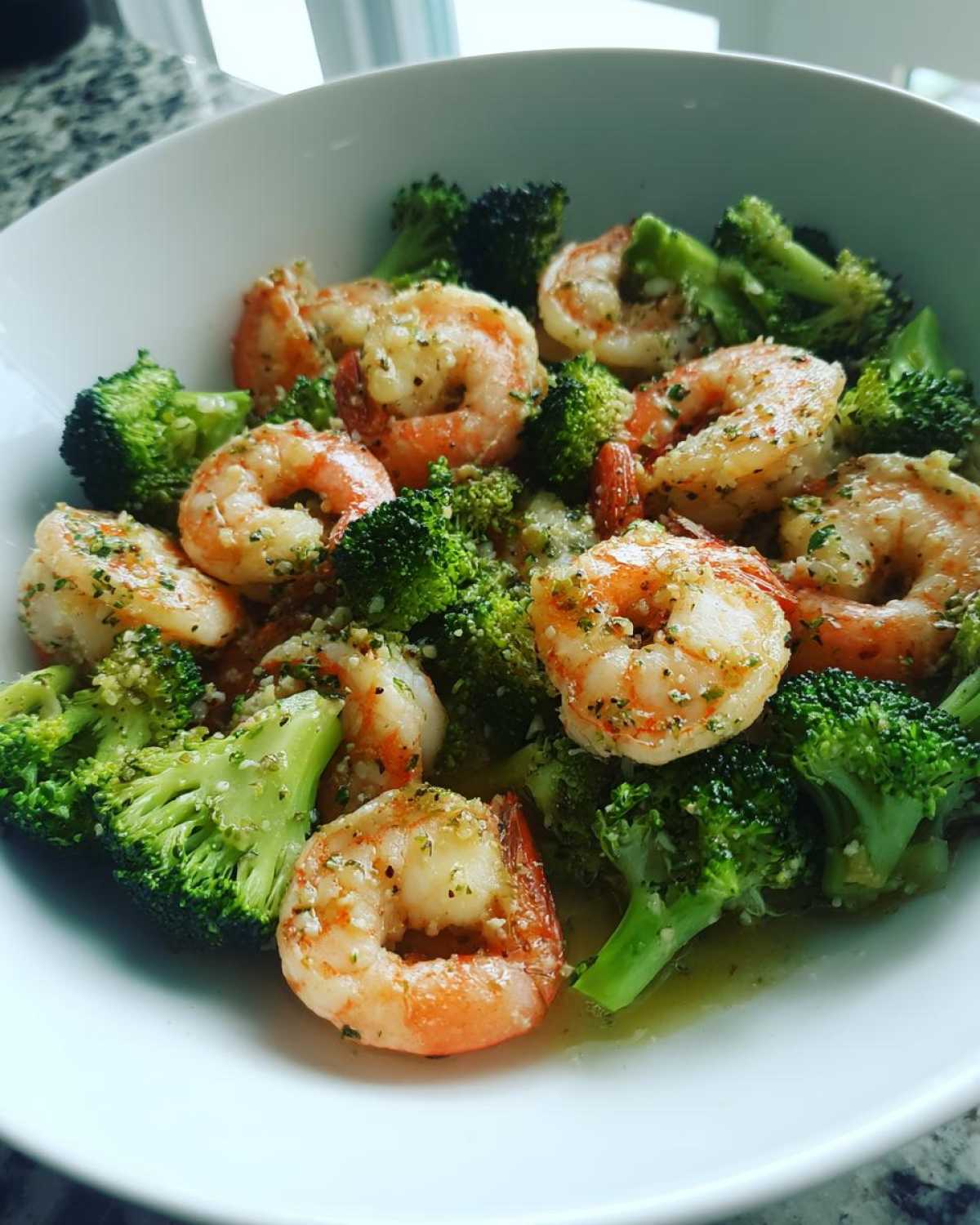 Close-up of cooked shrimp and bright green broccoli florets coated in garlic butter sauce, served in a white bowl.