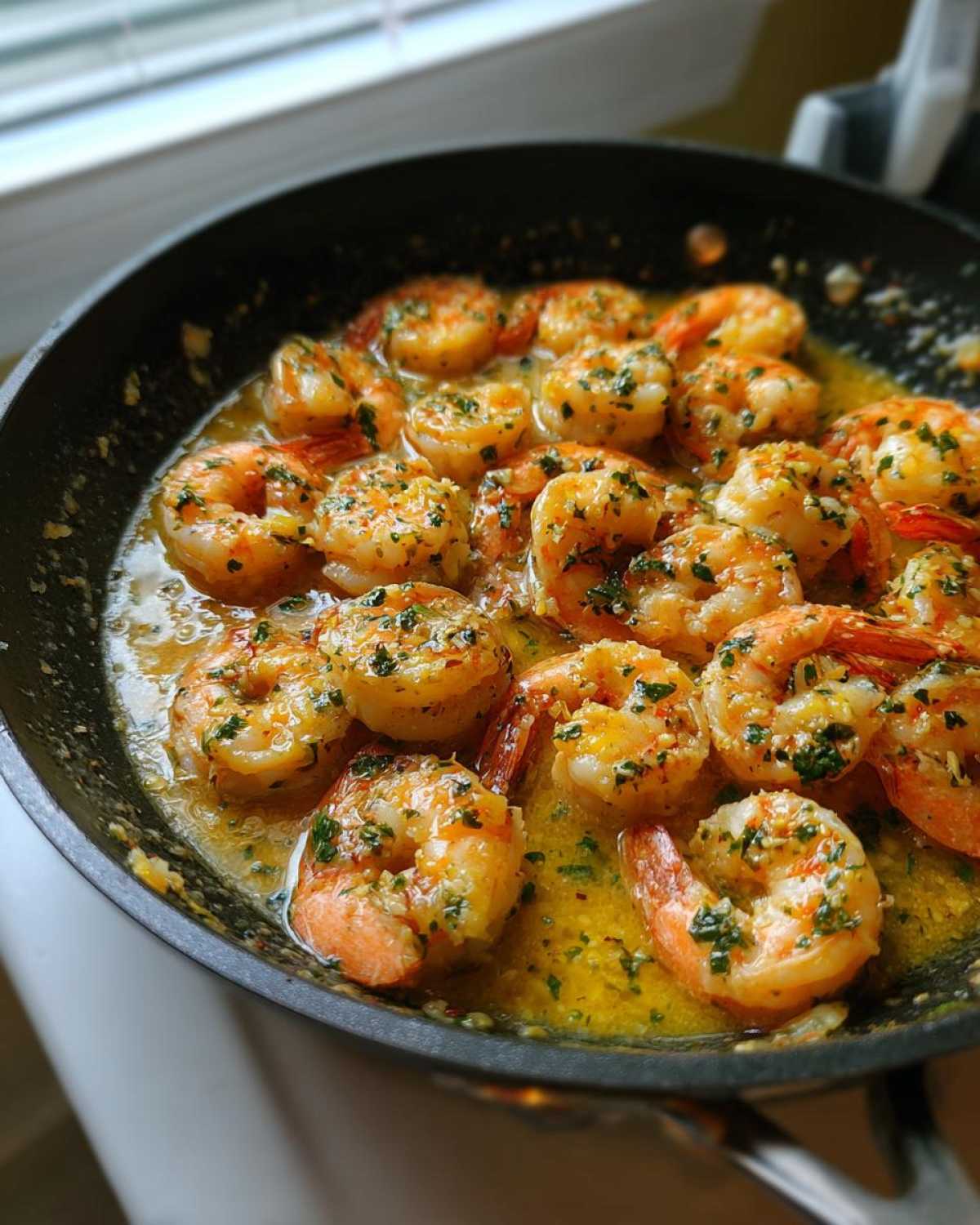 Close-up of cooked shrimp sizzling in a black skillet with rich garlic butter shrimp sauce and parsley.