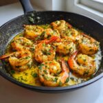 Close-up of plump shrimp sizzling in a black skillet coated in rich garlic butter shrimp skillet sauce with parsley.
