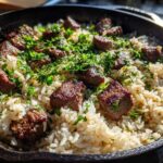 Close-up of Garlic Butter Steak and Rice Skillet Dinner topped with fresh parsley in a cast iron pan.