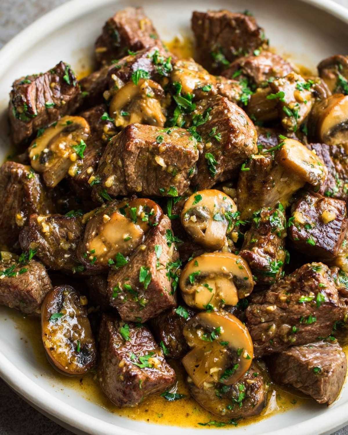 A close-up of tender Garlic Butter Steak Bites with Mushrooms coated in a rich garlic butter sauce and sprinkled with parsley.