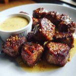 Close-up of juicy, caramelized Garlic Butter Steak Bites glistening with sauce, served with a side of creamy garlic sauce.
