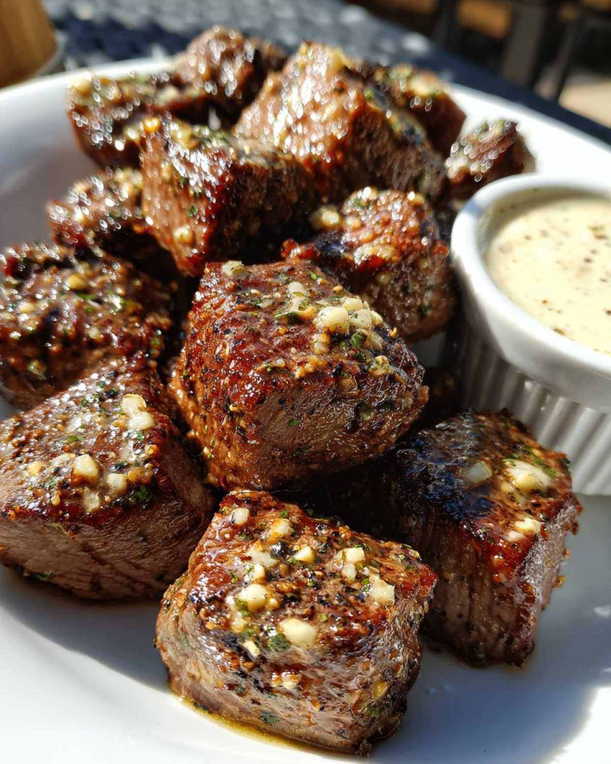 Close-up of seared Garlic Butter Steak Bites topped with minced garlic and herbs, served with a side of creamy garlic sauce.