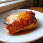 A close-up of a perfectly cooked piece of Honey Butter Chicken Skillet with golden, glossy edges sitting in sauce.