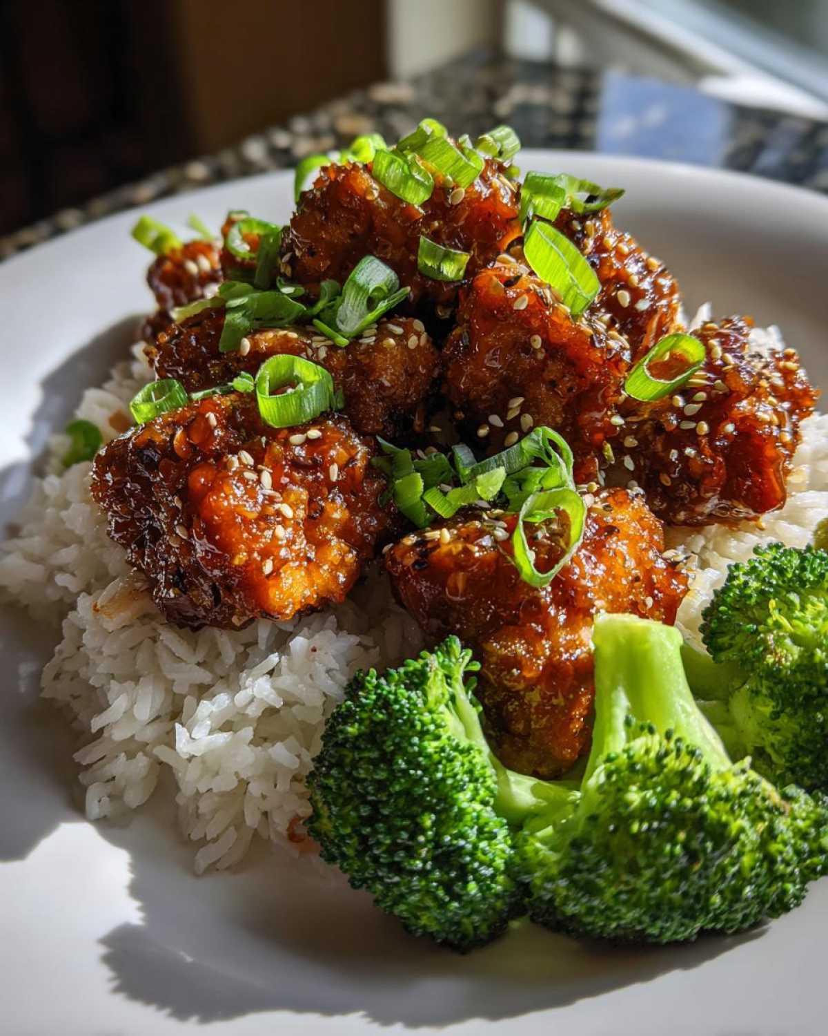 Close-up of Honey Garlic Chicken Bites glazed in sauce, served over white rice with steamed broccoli and green onions.