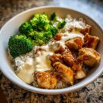 A close-up of a Honey Garlic Chicken Bowl featuring sticky glazed chicken pieces, white rice, steamed broccoli, and a drizzle of creamy sauce.
