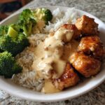 A close-up of a Honey Garlic Chicken Bowl featuring glazed chicken pieces, white rice, steamed broccoli, and a generous drizzle of creamy sauce.