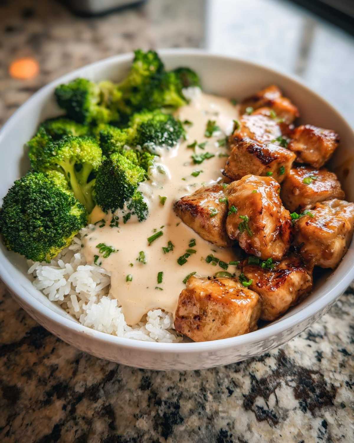 Close-up of a Honey Garlic Chicken Bowl featuring glazed chicken pieces, white rice, steamed broccoli, and a creamy sauce.