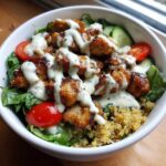 Close-up of a Honey Mustard Chicken Bowl featuring glazed chicken pieces, creamy sauce, quinoa, lettuce, tomatoes, and cucumber.