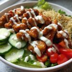 Close-up of a Honey Mustard Chicken Bowl featuring glazed chicken pieces drizzled with creamy sauce, cucumbers, tomatoes, and quinoa.