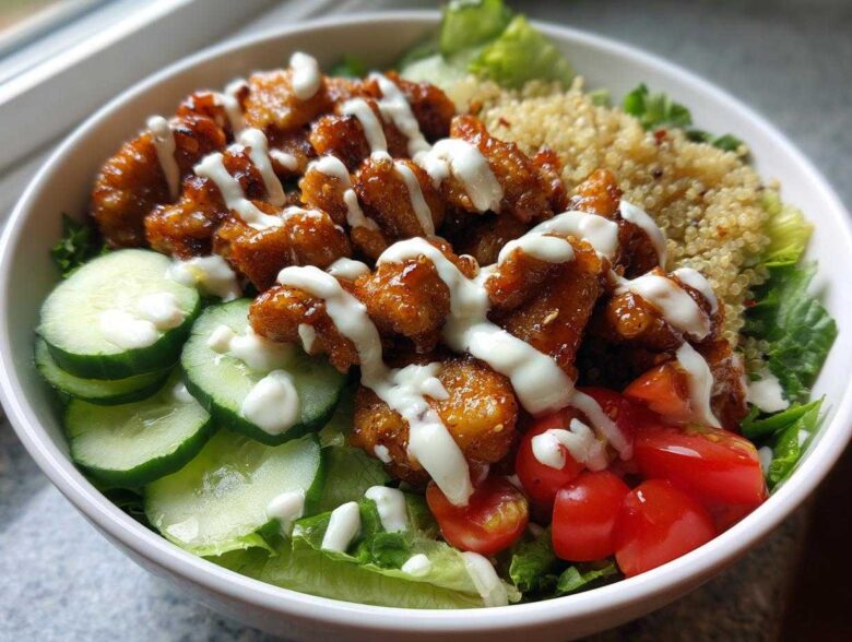 Close-up of a Honey Mustard Chicken Bowl featuring glazed chicken pieces drizzled with creamy sauce, cucumbers, tomatoes, and quinoa.