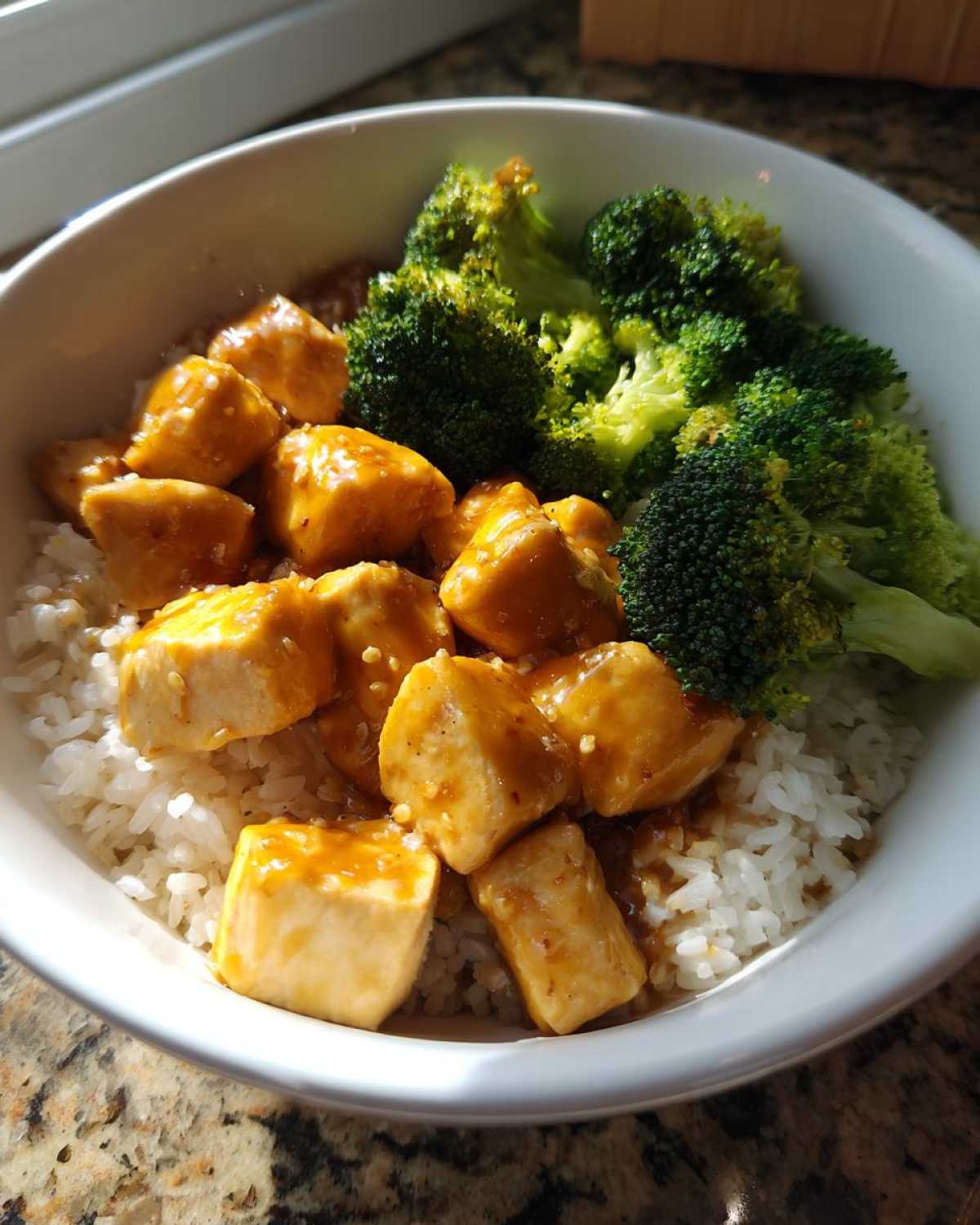 A white bowl filled with Honey Mustard Chicken Bowl with Rice, topped with chunks of glazed chicken and steamed broccoli florets.