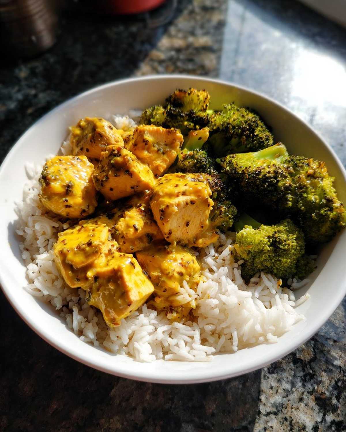 A white bowl filled with Honey Mustard Chicken Bowl with Rice, topped with chunks of yellow honey mustard chicken and roasted broccoli florets.
