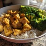 A close-up of a Honey Mustard Chicken Bowl with Rice, featuring cubed chicken coated in sauce next to bright green steamed broccoli.