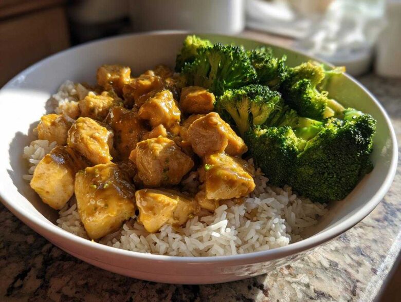 A close-up of a Honey Mustard Chicken Bowl with Rice, featuring cubed chicken coated in sauce next to bright green steamed broccoli.