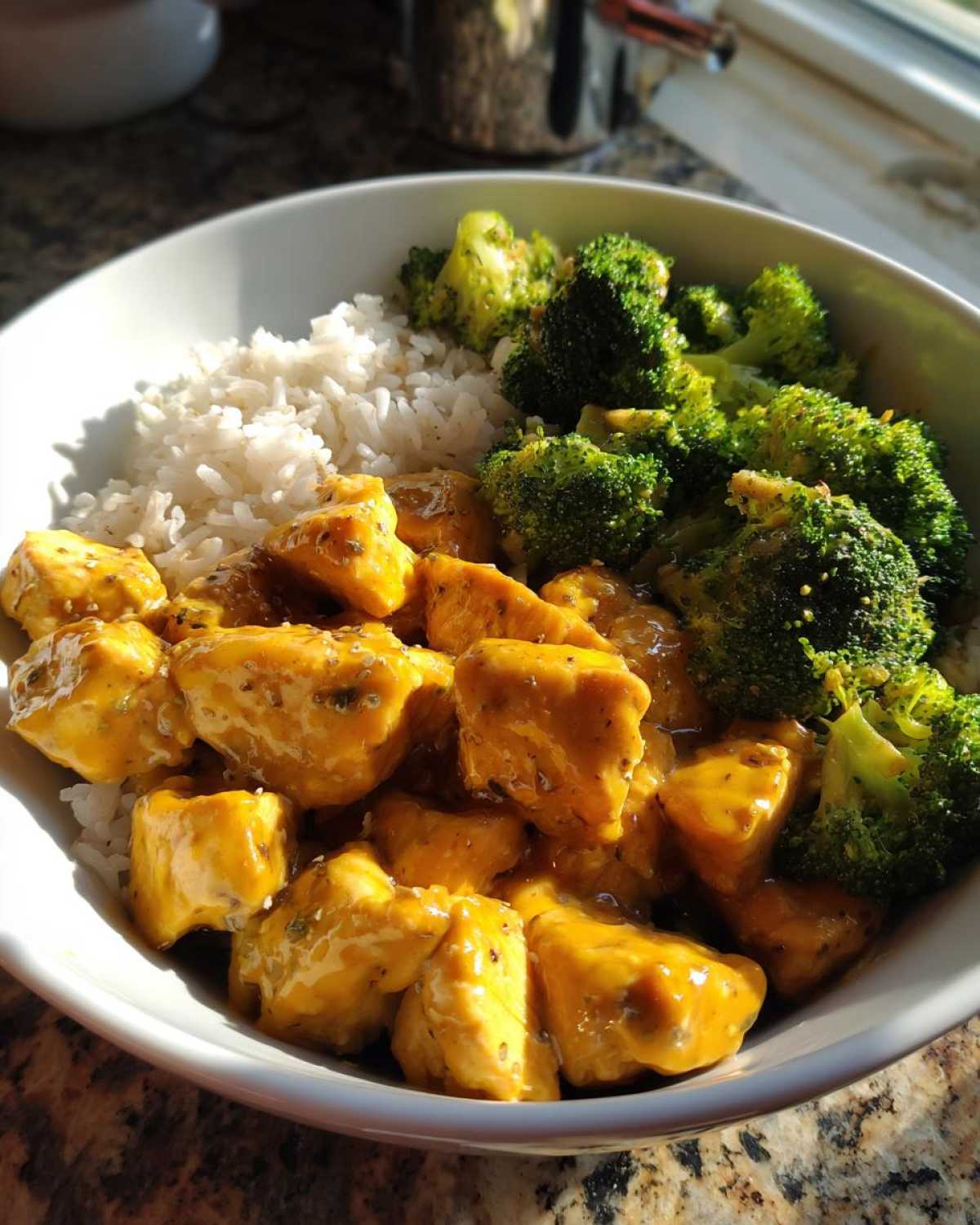Close-up of a Honey Mustard Chicken Bowl with Rice, featuring chunks of chicken in a yellow sauce, white rice, and bright green broccoli florets.