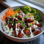 Close-up of a Honey Soy Chicken Bowl featuring glazed chicken pieces over rice, topped with garlic sauce, scallions, and sesame seeds.
