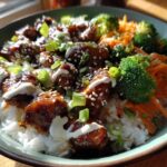 A close-up of a Honey Soy Chicken Bowl featuring glazed chicken pieces over white rice, topped with broccoli, carrots, and a drizzle of white sauce.