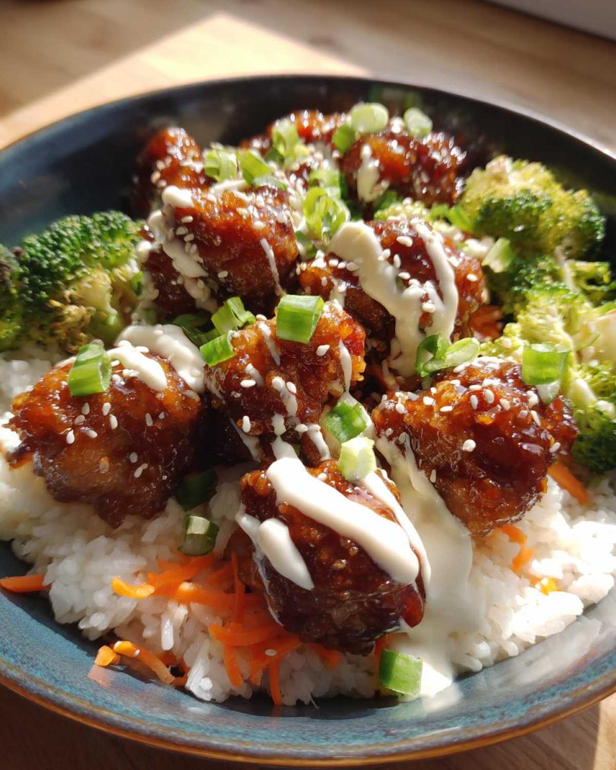 Close-up of a Honey Soy Chicken Bowl featuring glazed chicken pieces over rice, broccoli, carrots, and drizzled with white garlic sauce.
