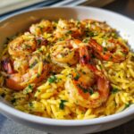 A close-up of a white bowl filled with Lemon Garlic Shrimp Orzo One Pan Dinner, topped with seasoned shrimp and fresh parsley.