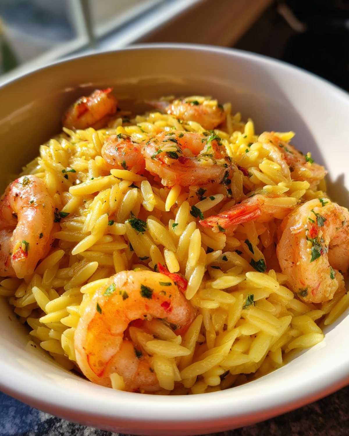 Close-up of Lemon Garlic Shrimp Orzo pasta topped with seasoned shrimp and fresh parsley in a white bowl.