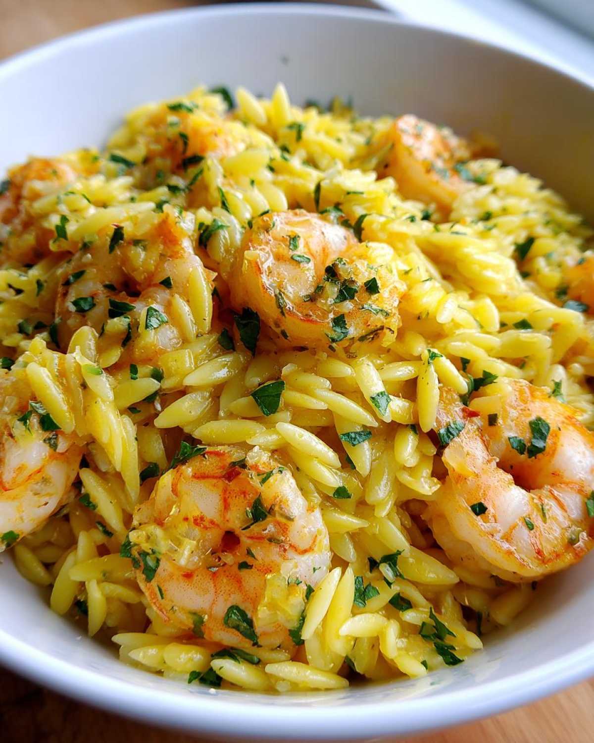 Close-up of a white bowl filled with Lemon Garlic Shrimp Orzo, garnished with fresh parsley.